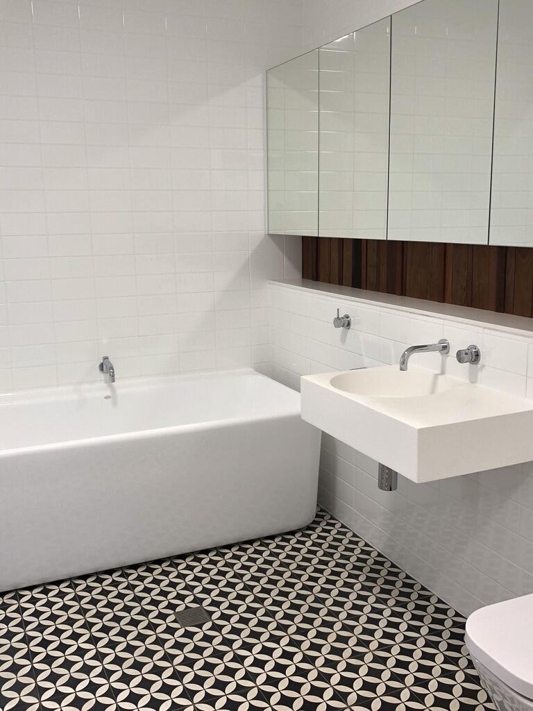 Modern architect designed bathroo with Jatana floor tiles, white wall tile, back to wall bath and wall-hung basin, mirrored vanity cupboards