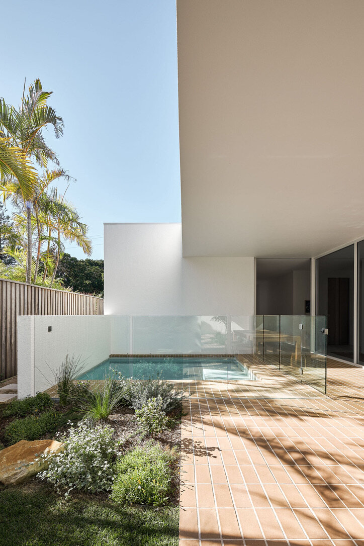 Modern architect designed white rendered house with pool and frameless glass pool fence, brick pavers