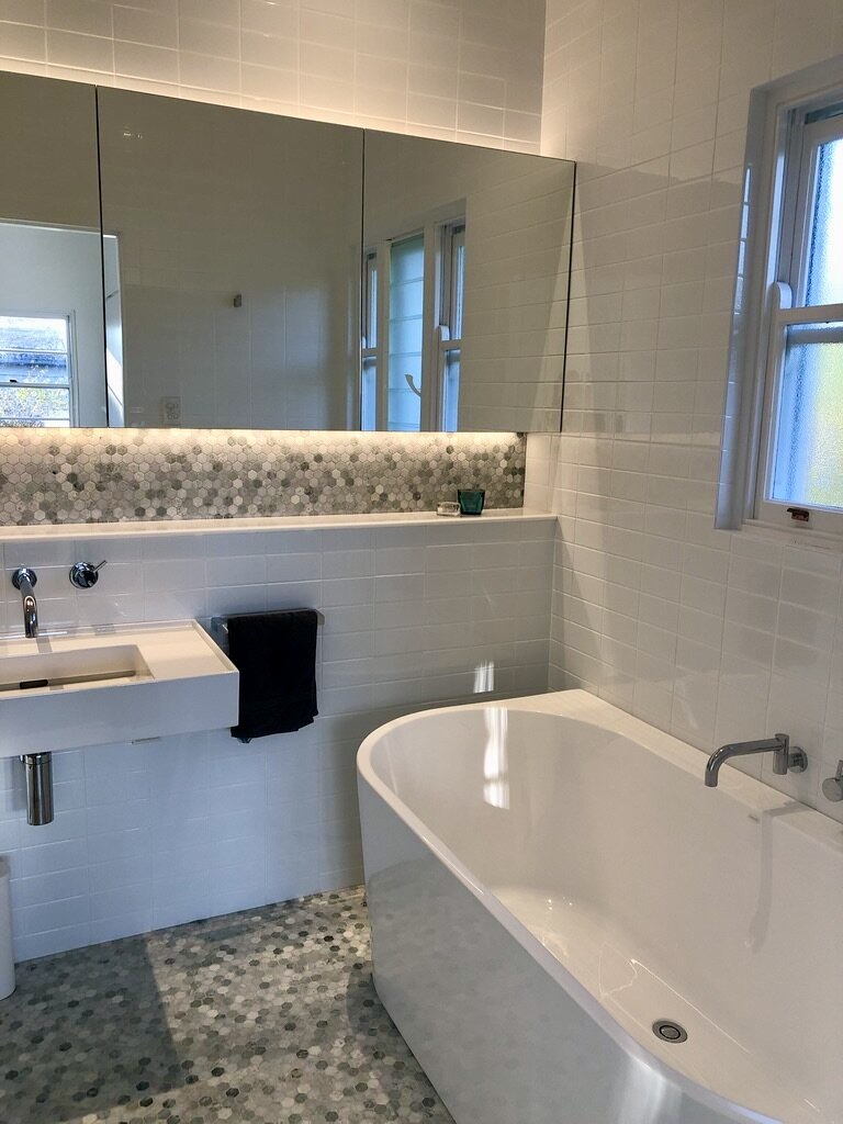 Modern architect designed bathroom back to wall bath, green marble mosaic tiles with glass vanity cupboards and wall hung basin