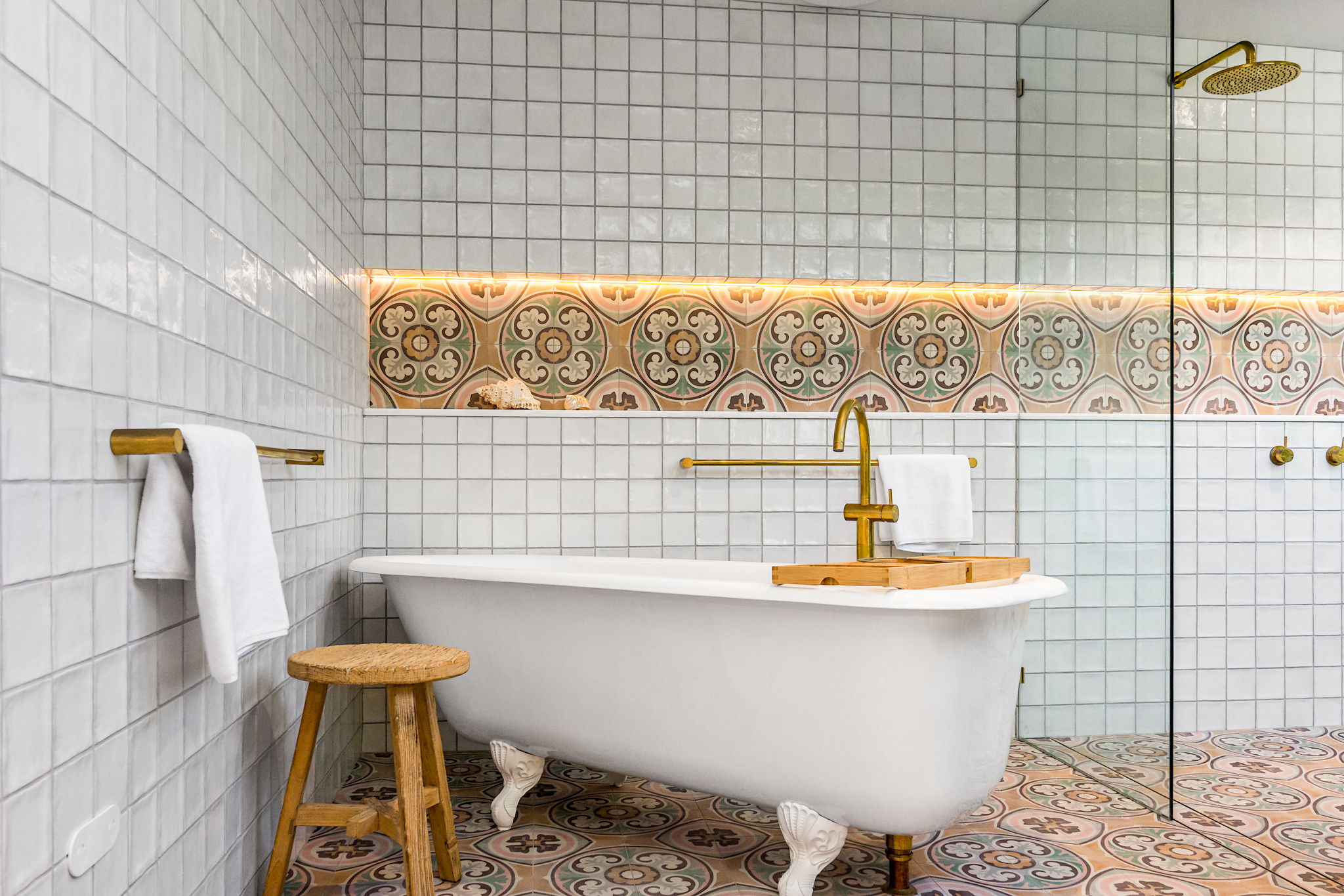 Modern architect designed bathroom with claw foot bath, aged brass tapware, niche with decorative inset tile.
