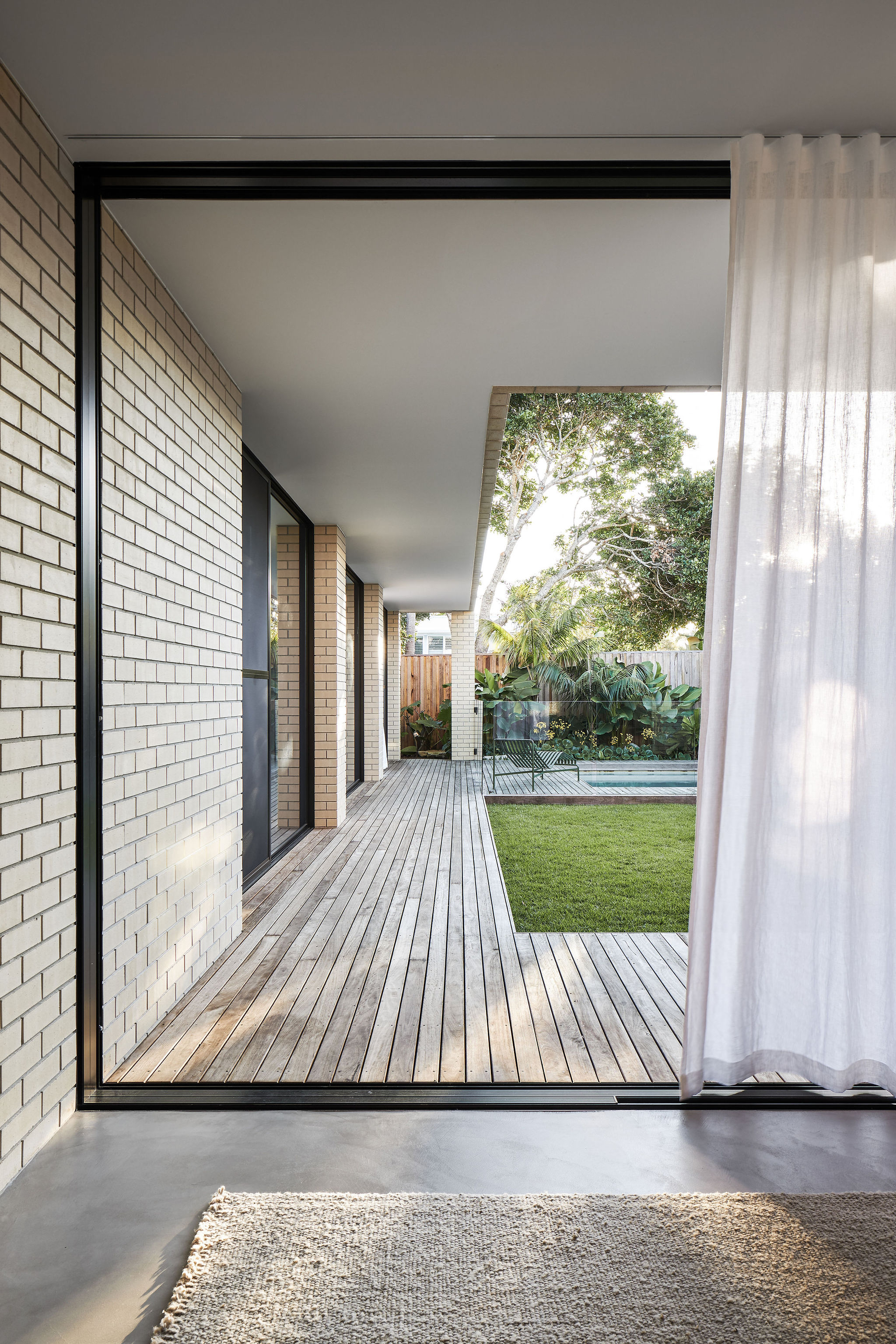 Modern architect designed house timber deck large sliding doors looking out to lawn and pool, cream face brick walls