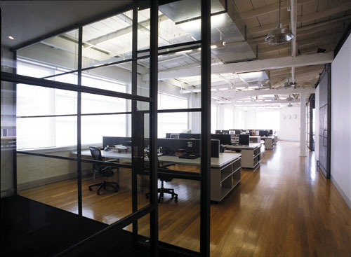 Modern architect designed office with steel framed glass walls and long desks with low screens, sliding metal barn door