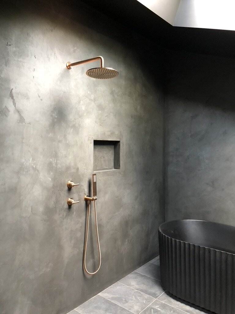 Modern architect designed bathroom with dark microcement  rendered walls, copper finish fittings and black scalloped free-standing bath