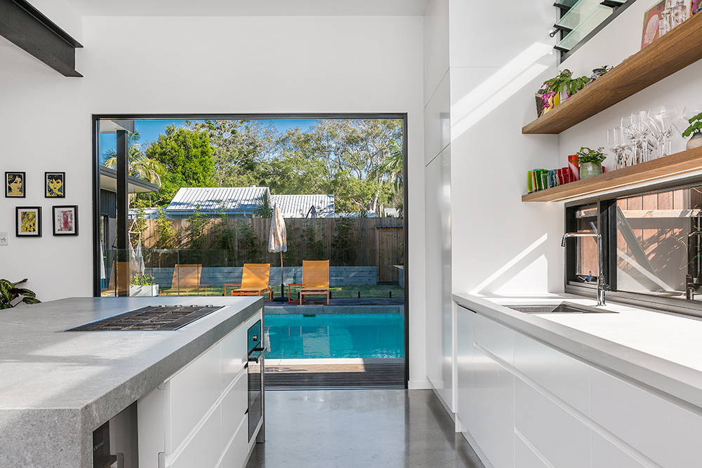 Modern architect designed residence white kitchen, open shelves, concrete floor with a large picture window looking to the pool.
