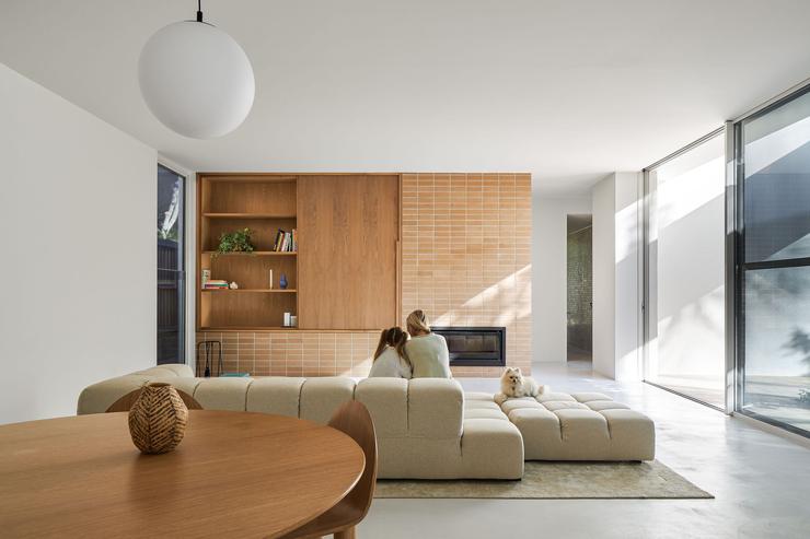 Living room of modern architect designed home with white walls, face brick and timber veneer joinery unit with fireplace. Mother and child sitting on cream modern sofa.