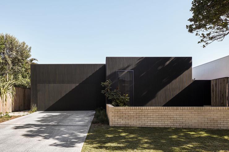 Front view of modern architect designed house with black vertical timber slats and cream brick front wall